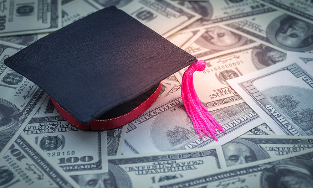 A graduation cap sits atop a pile of $100 bills.