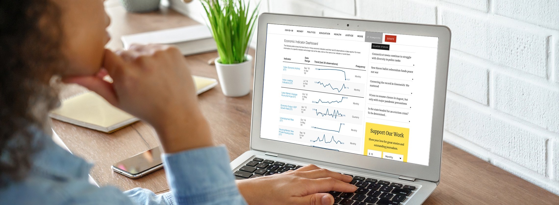 A woman using a laptop that is open with the Economic Indicator Dashboard on the screen.