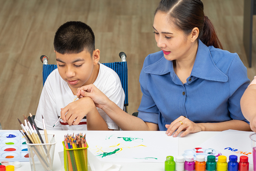 A student with disabilities takes part in an art class with a teacher.